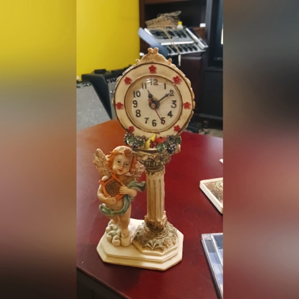 Vintage Angel clock. Angel is playing a harp. Clock is on a pedalestal.
